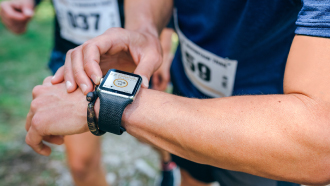 Braço de homem com smartwatch num pulso e a outra mão a mexer nele depois de uma corrida.